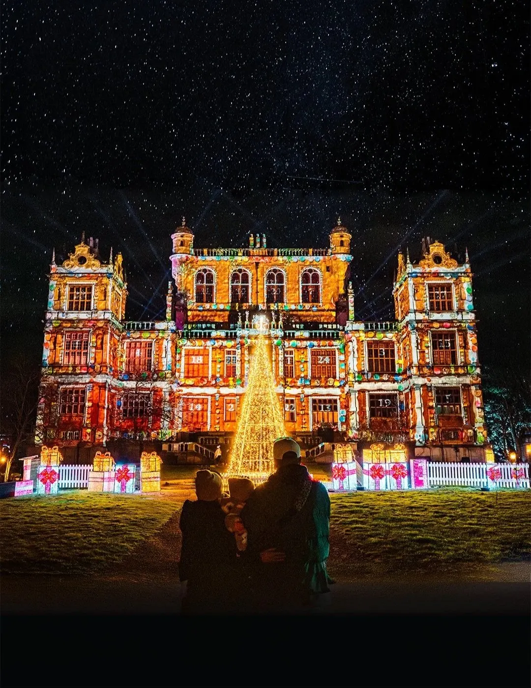 Wollaton Hall facade lit with colourful projections and family silhouettes on the Winter Light Trail