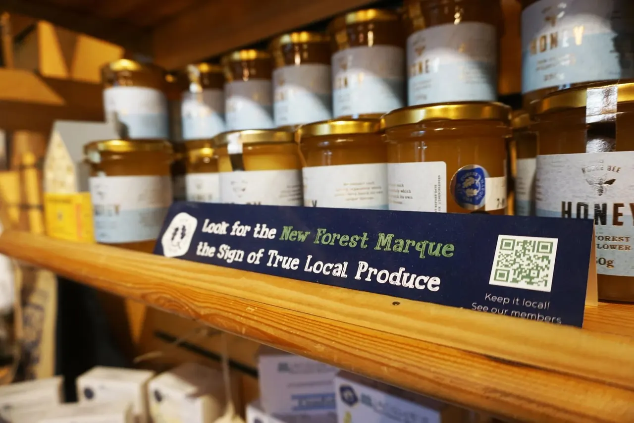 Shelf display of local honey and preserves in jars with a New Forest Marque sign promoting local produce.