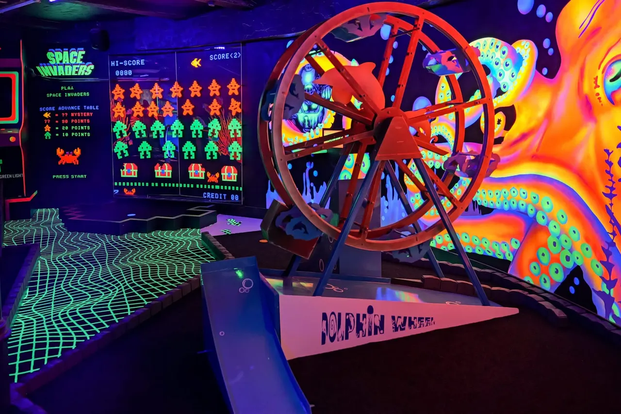 Retro arcade gaming area with neon-lit Space Invaders cabinet and a red Dolphin Wheel game machine under purple lighting.