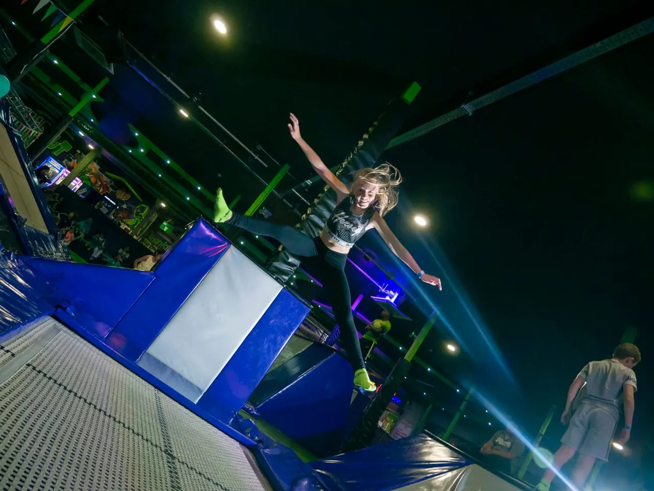 Young woman bouncing on an inflatable trampoline attraction at an indoor play centre at night.