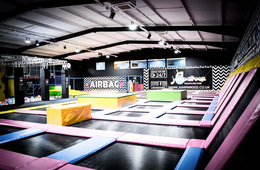 Indoor trampoline park with colourful padded jumping surfaces, foam obstacles, and inflatable structures under bright ceiling lights.