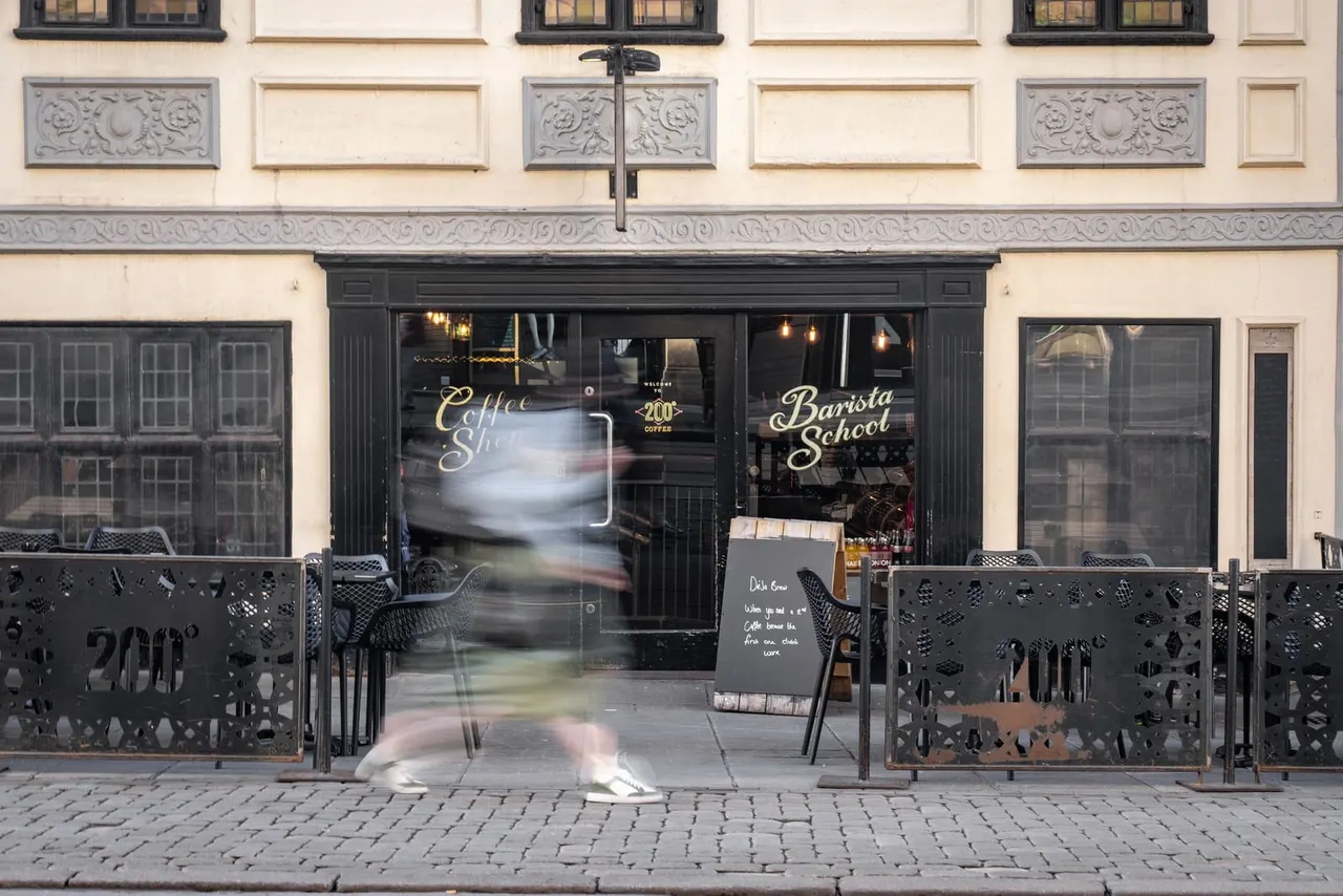 Storefront of a coffee shop with black-framed windows and cream-coloured facade, metal outdoor seating on pavement.
