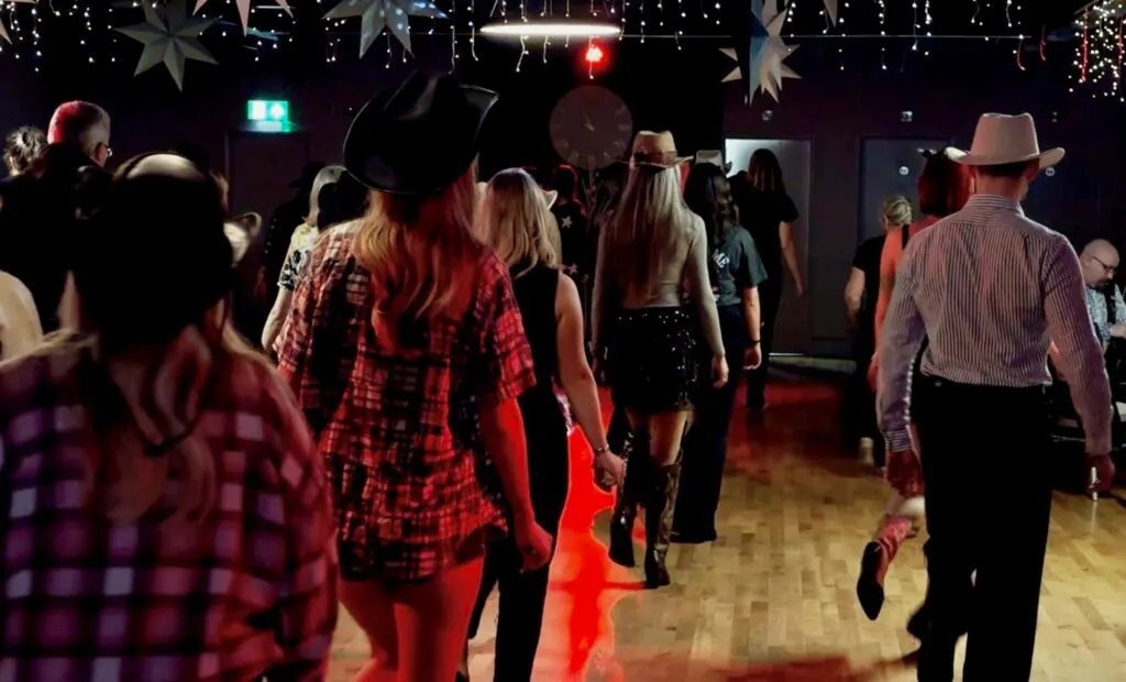 People dancing and mingling on a lit dancefloor beneath hanging stars and festive decorations in a dark venue.