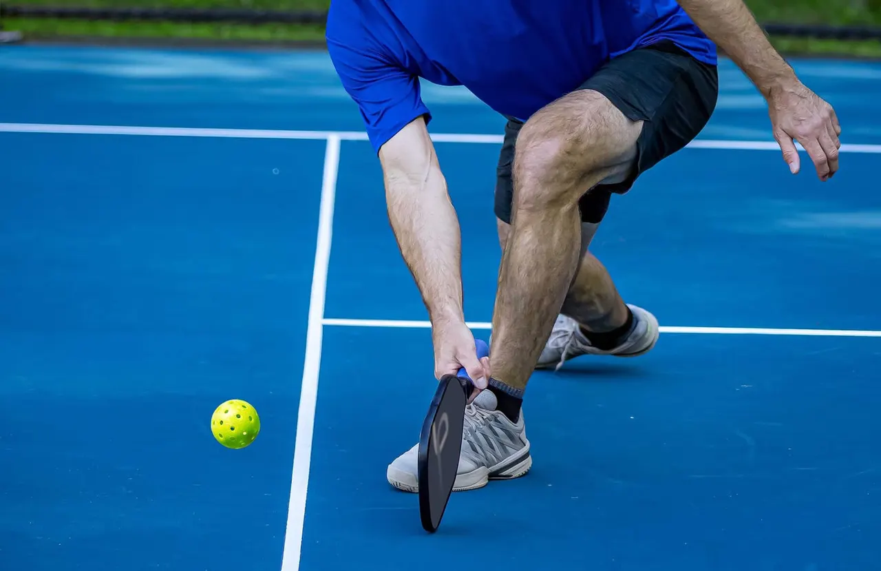 Man in blue shirt playing pickleball on blue court, holding paddle near yellow ball.