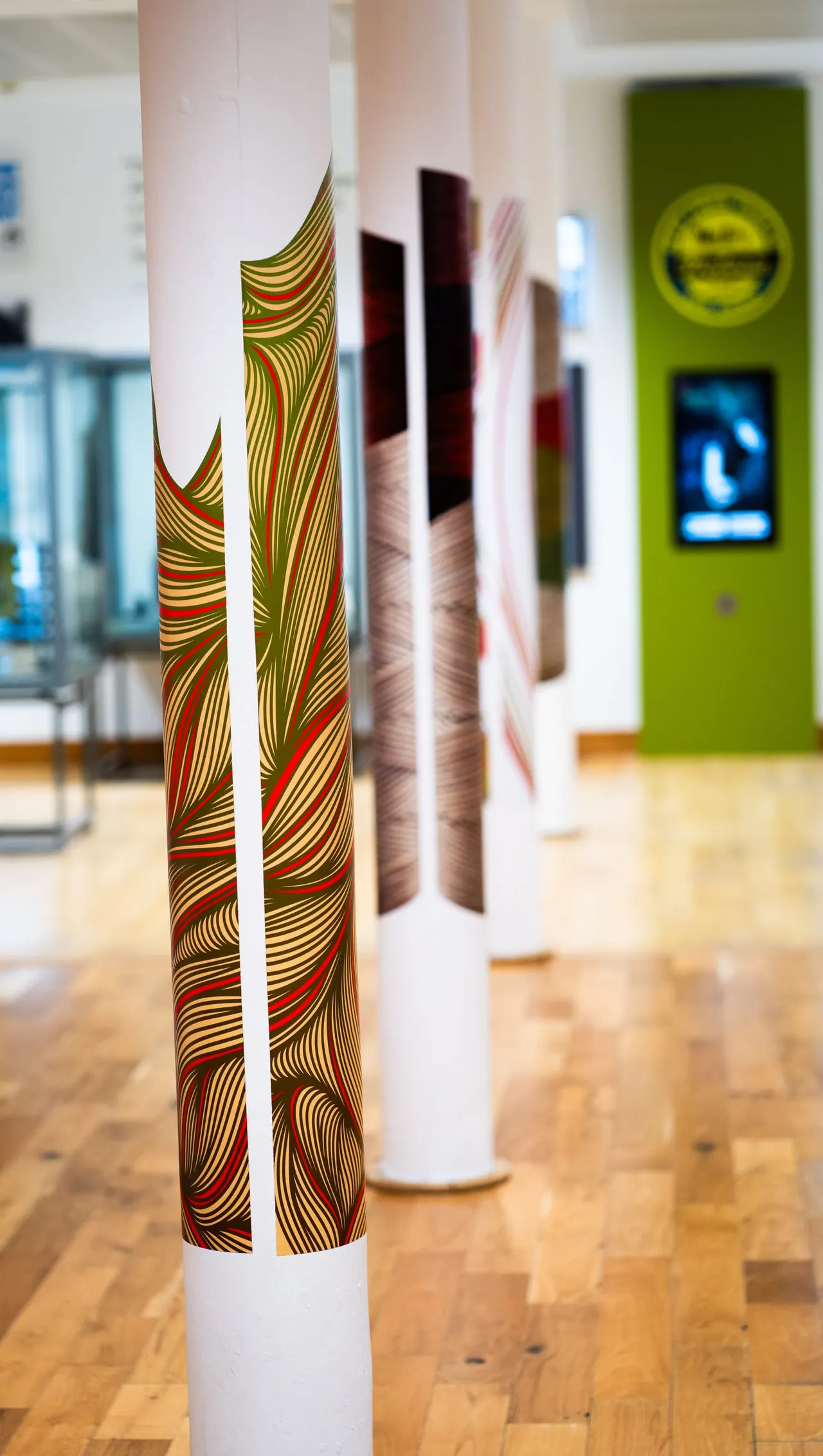 A row of cylindrical columns wrapped in vibrant patterned fabric with red, gold and green stripes displayed indoors.