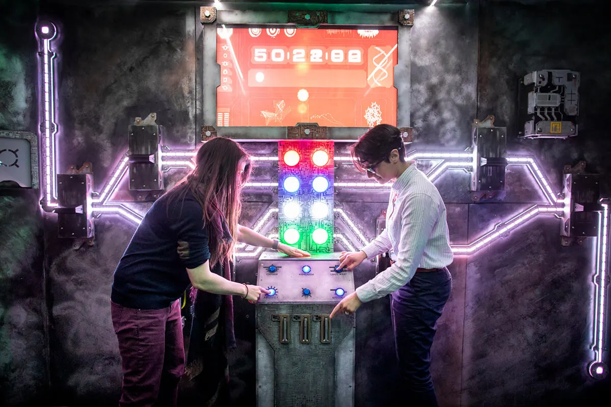 Two people playing an arcade game surrounded by neon purple lighting and a red display screen showing a score.