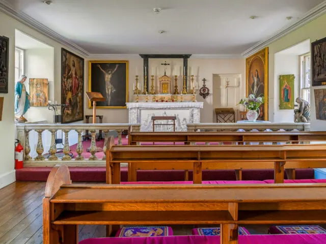 Interior of a chapel with wooden pews, ornate altar, religious artwork and statues.