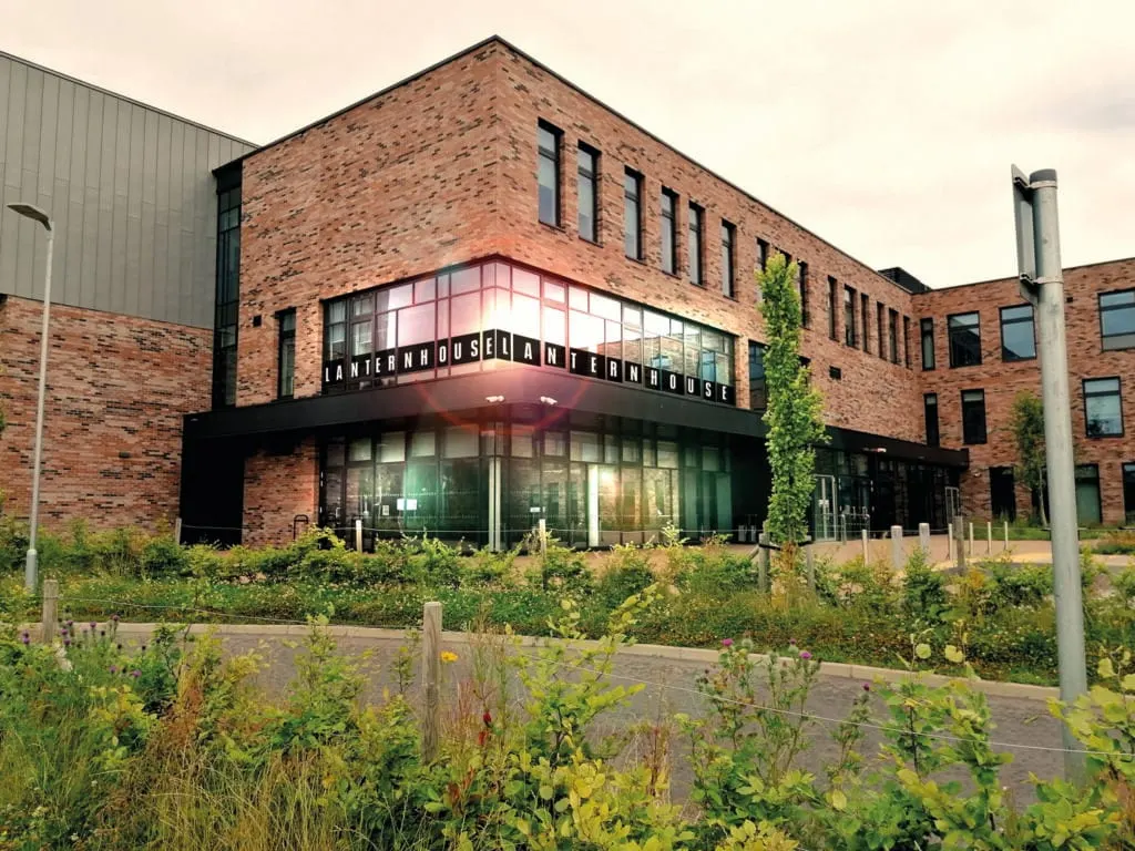 Modern brick building with signage reading "Lanternhouse" featuring large windows and surrounding landscaped gardens with shrubs.