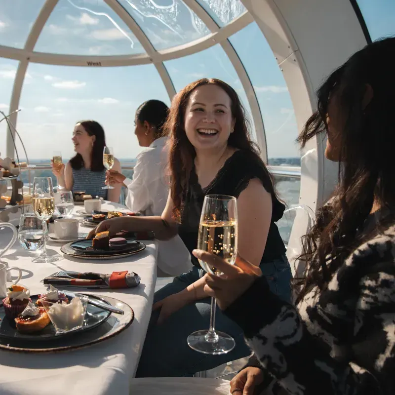 People dining at a table inside a high-rise observation pod with panoramic city views.