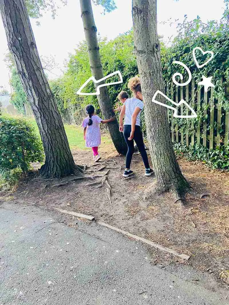 Two children walking between large trees on a woodland path with white drawn arrows and hearts overlaid.
