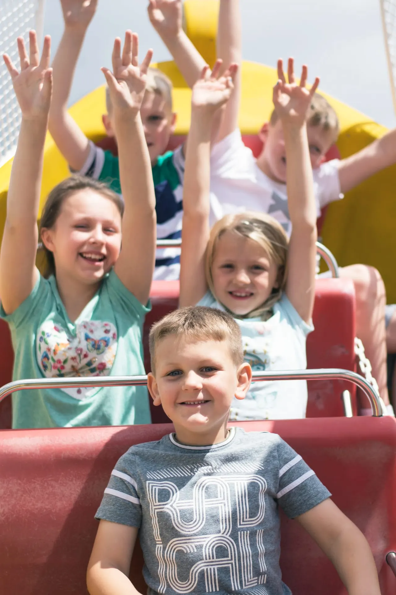 Children on a fairground ride with their hands raised in the air, smiling and enjoying themselves.