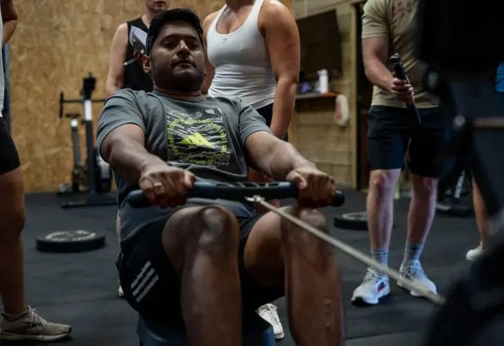Man performing a rowing exercise with a cable machine whilst other gym members watch in a fitness studio.