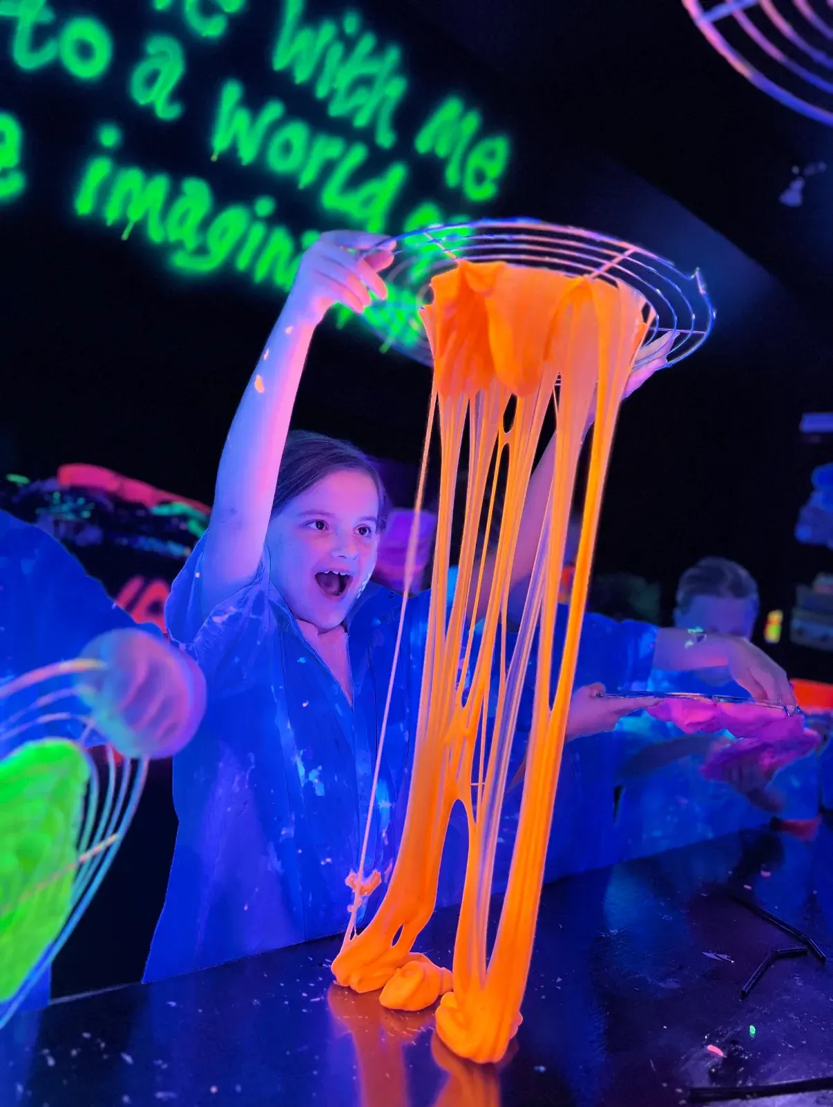 Child playing with glowing fluorescent slime under ultraviolet light at an interactive activity.