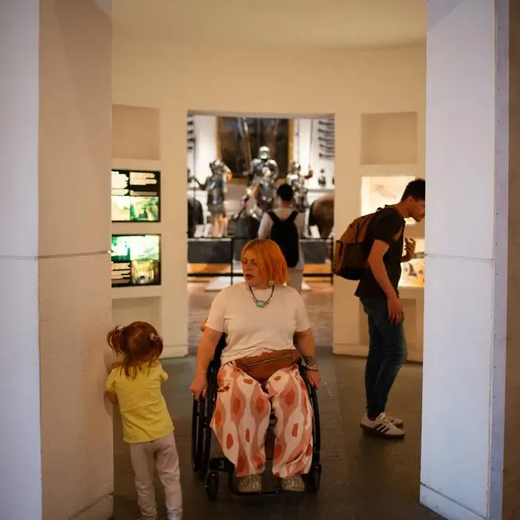 Woman in wheelchair and child in yellow shirt viewing museum exhibits with sculptures visible in background.