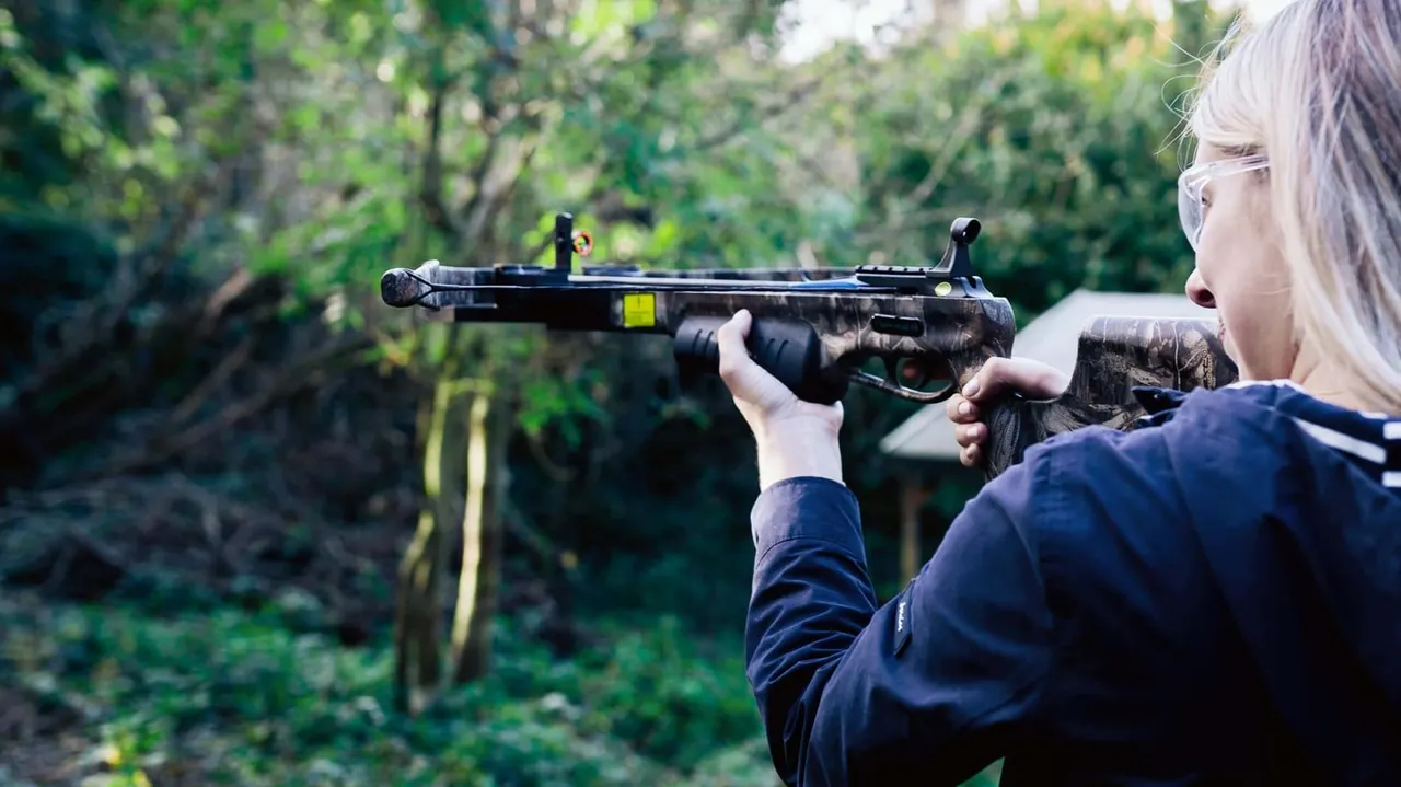 Person aiming an air rifle at a target in a wooded outdoor setting.