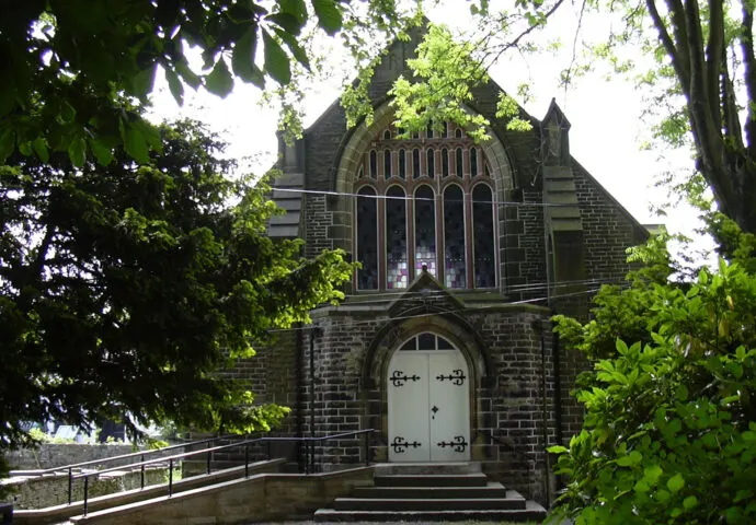 Historic stone chapel with ornate Gothic windows surrounded by green foliage and trees.