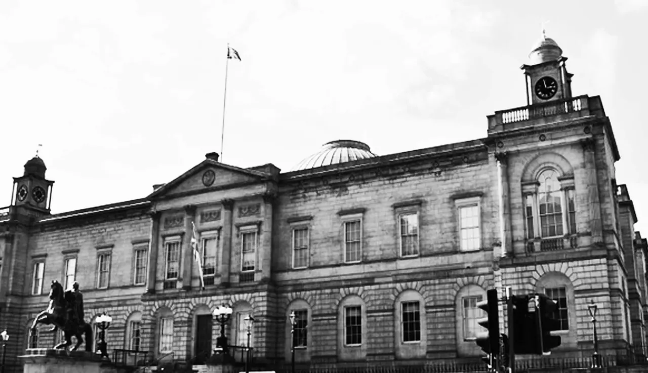 Historic stone civic building with clock towers and equestrian statue in front.