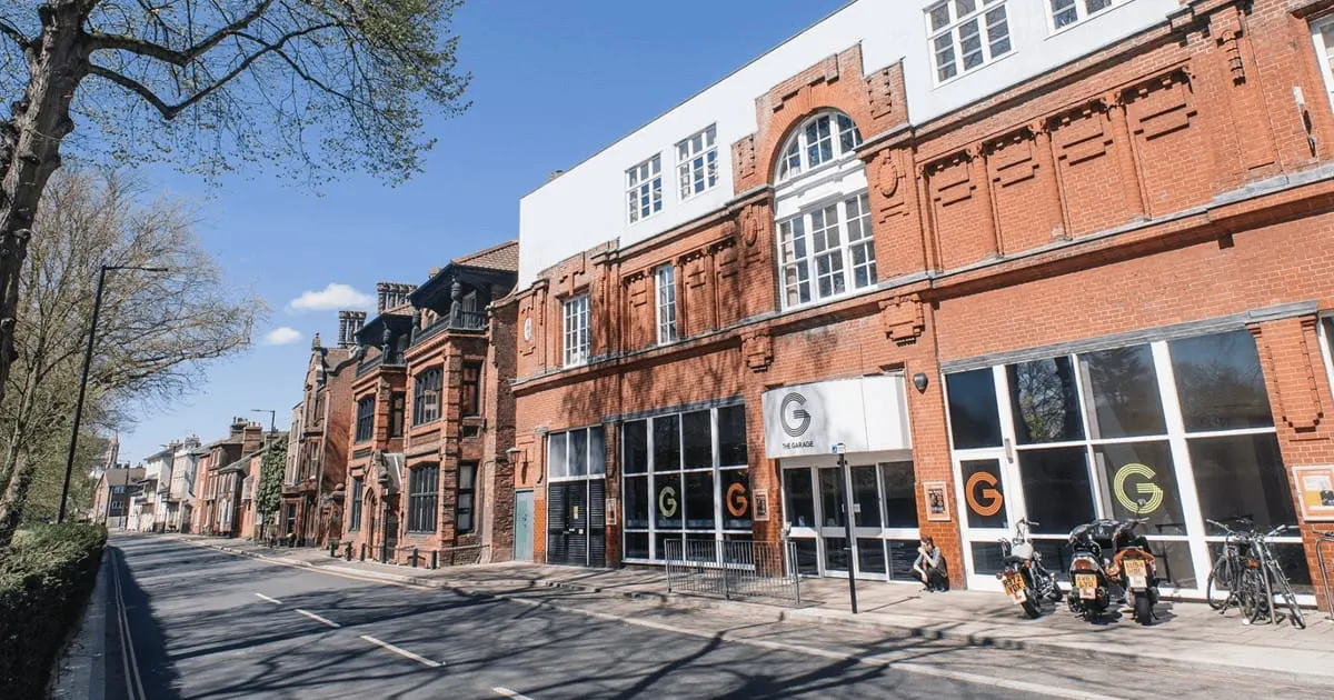 Victorian brick buildings converted into a leisure venue with large shop windows, motorcycles and bicycles parked outside on a sunny day.