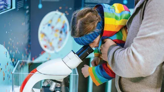 Child looks through a microscope whilst holding a colourful Rubik's cube.