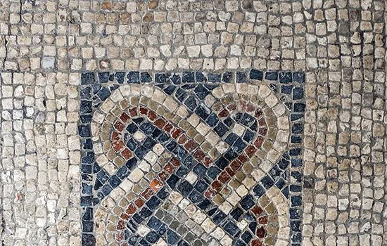 Ancient Roman mosaic floor showing geometric patterns in cream, brown and dark blue tesserae.