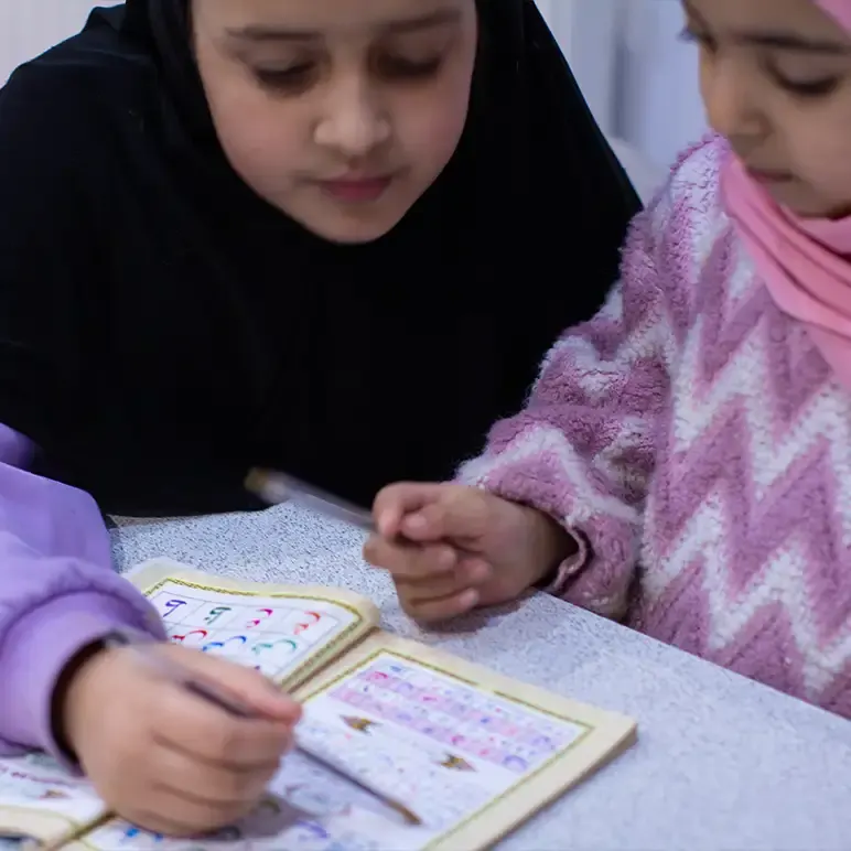 Two young children reading together from an open book at a table.