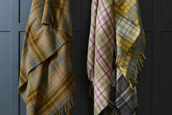 Tartan blankets in gold and purple checks hanging against a dark panelled wall.