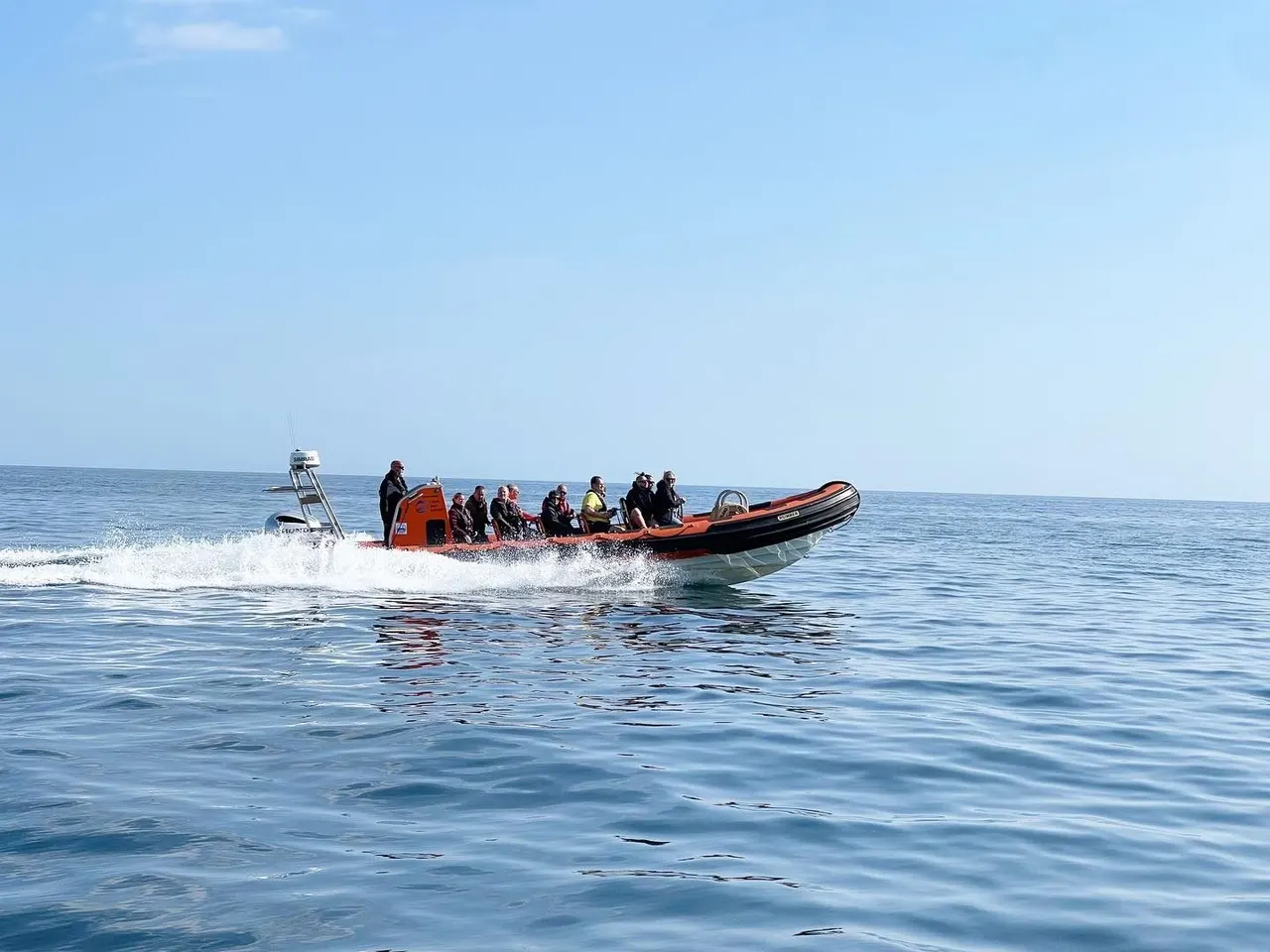 A speedboat full of passengers approaches the shore through shallow waves on a clear day.