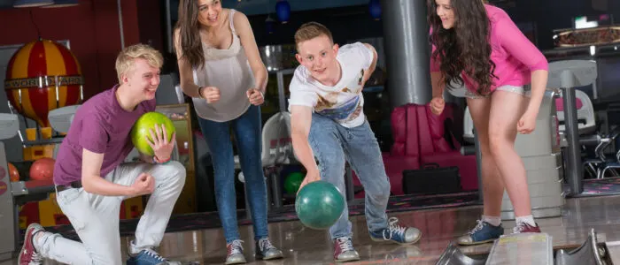 Young people bowling together in an indoor bowling alley with colorful balls and pins visible.