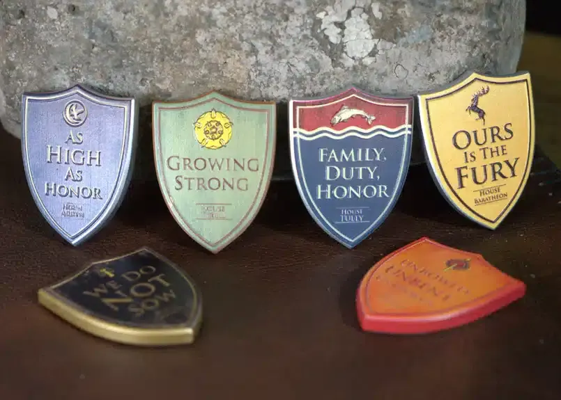 Six decorative shield plaques with House mottos from the fictional series displayed against a stone wall.