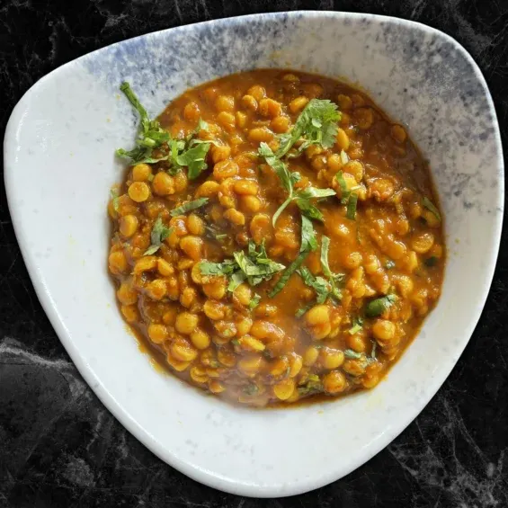 Bowl of spiced chickpea curry garnished with fresh coriander, served in a white bowl.