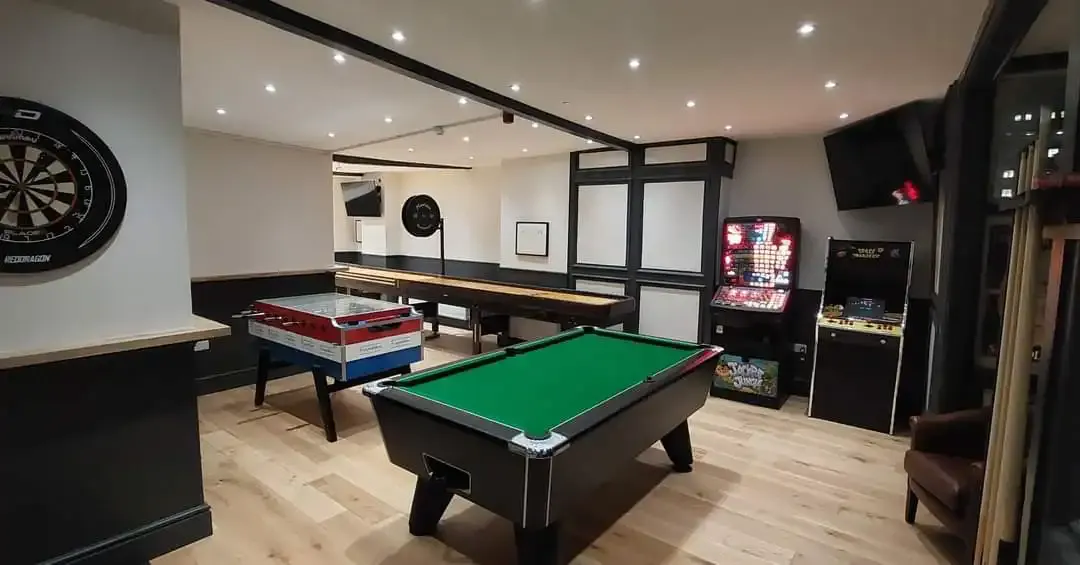 Indoor games room with pool table, arcade machines, darts board and air hockey table.