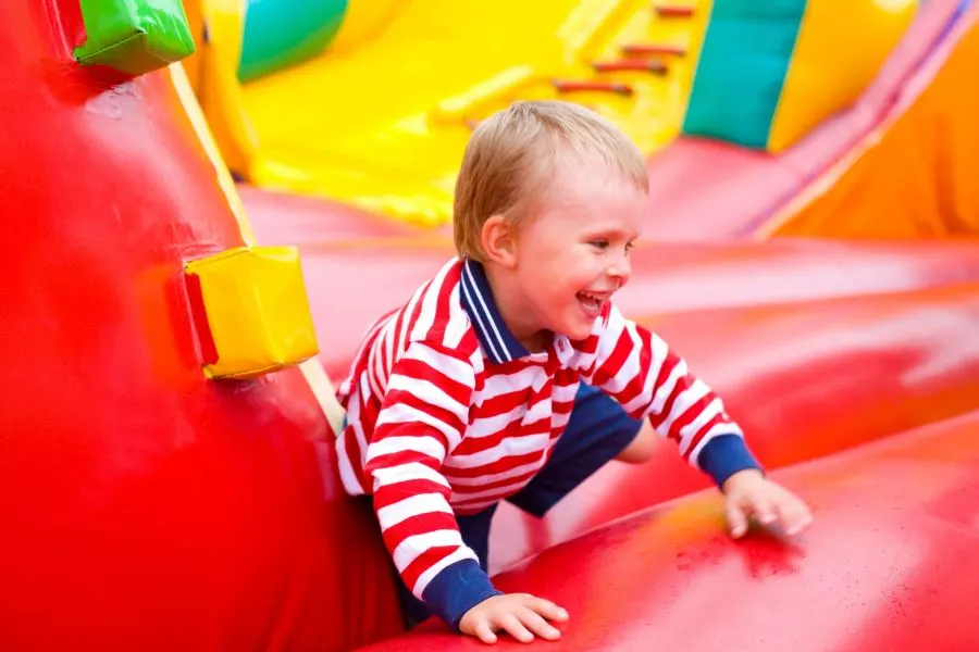 Young child in striped top playing on a brightly coloured inflatable bouncy castle.