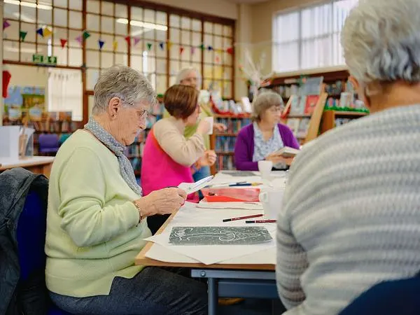 Older adults engaged in an art or craft activity at a table in a community room with colourful decorations.