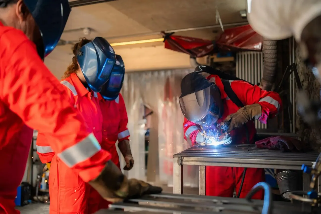 People in red protective suits and welding helmets practising welding techniques indoors.