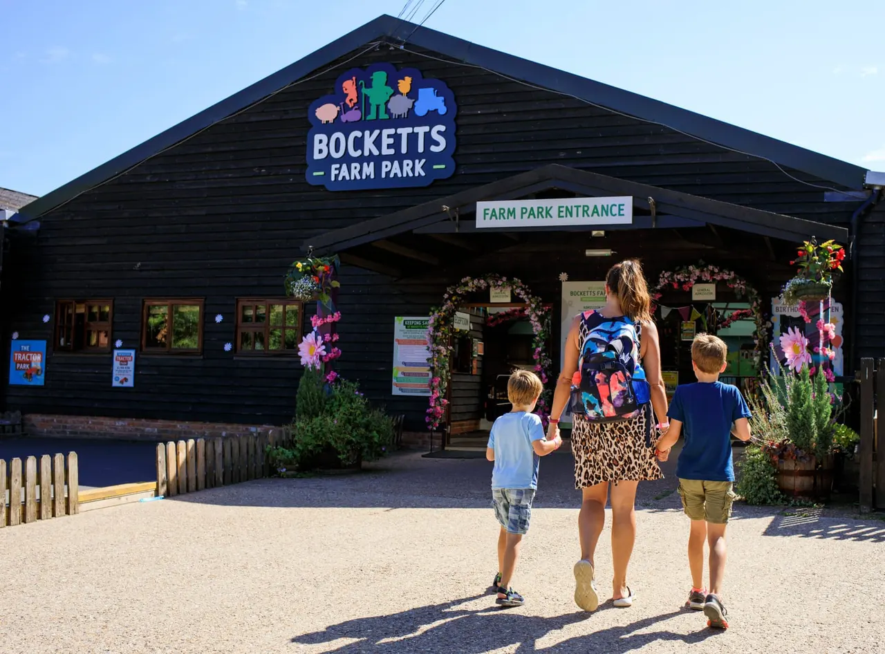An adult and two young children approach the farm park entrance building on a sunny day.
