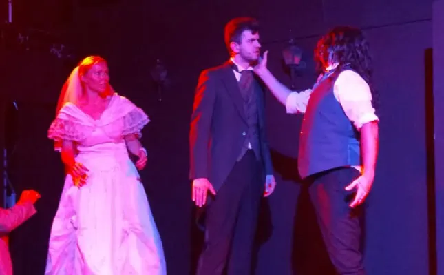 Three performers on stage under red and purple lighting during a theatrical production.