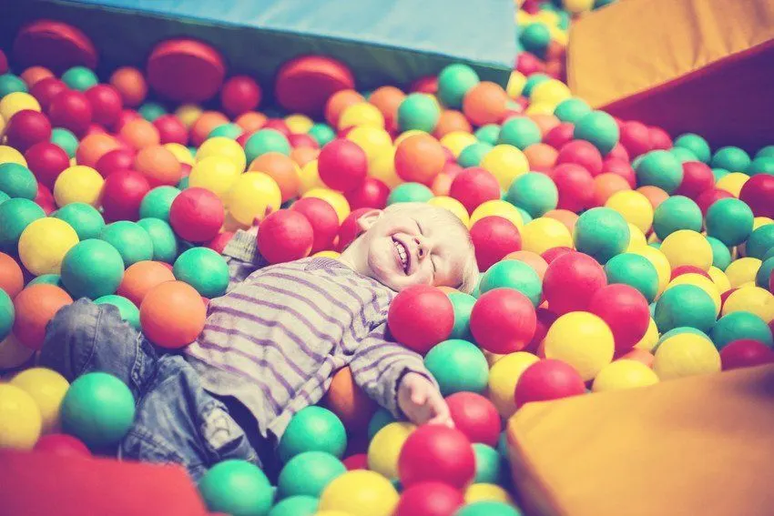 Child lying in a colourful ball pit filled with red, yellow, green and orange plastic balls.