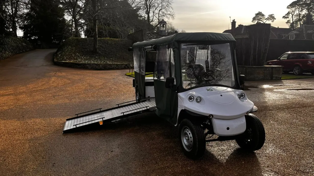 An adapted electric buggy with wheelchair ramp lowered, parked on a driveway at a country estate.