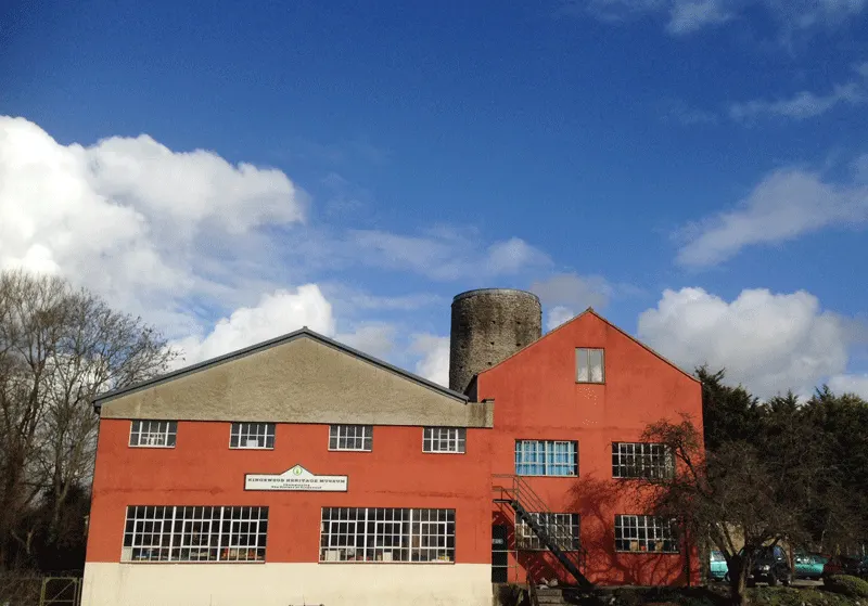Red-brick and cream heritage building with round stone tower against blue sky with white clouds.