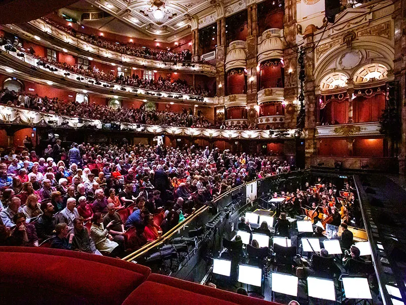 Ornate theatre auditorium filled with audience members watching a performance from multiple levels of seating.
