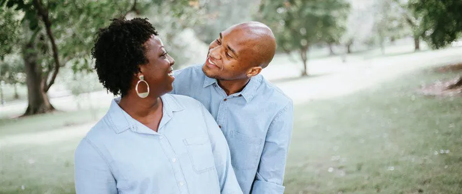 Two people smiling together in a tree-lined park setting.