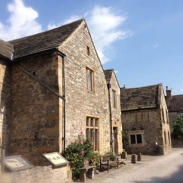 Stone-built historic house with multiple gabled roofs and windows, flowering plants outside, under blue sky.