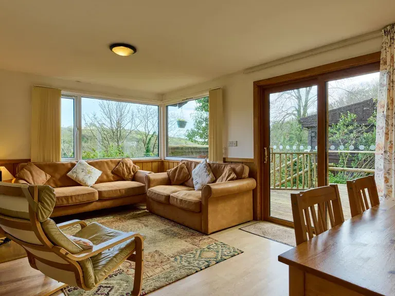 Spacious living room with tan leather seating, large windows overlooking countryside, and access to a balcony with rural views.