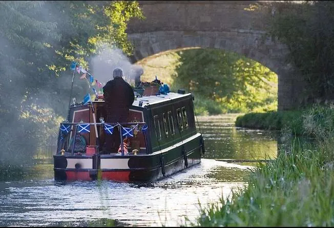 A narrowboat with passengers travels through a canal tunnel beneath a stone arch bridge.