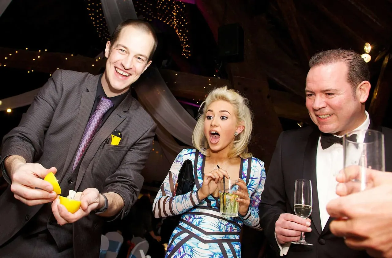 Three guests in formal attire enjoying drinks and entertainment at an indoor venue decorated with golden fairy lights.