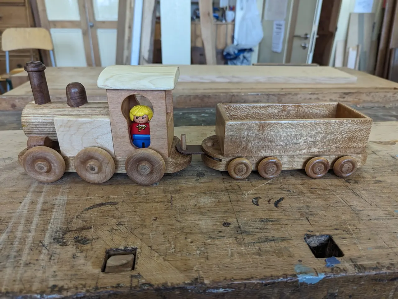 Wooden toy train set with engine and cargo car on a workshop table.