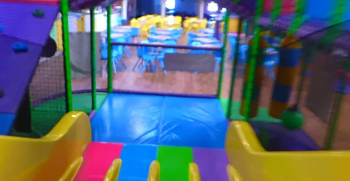 Colourful indoor play area with ball pit, slides and foam structures in bright neon lighting.