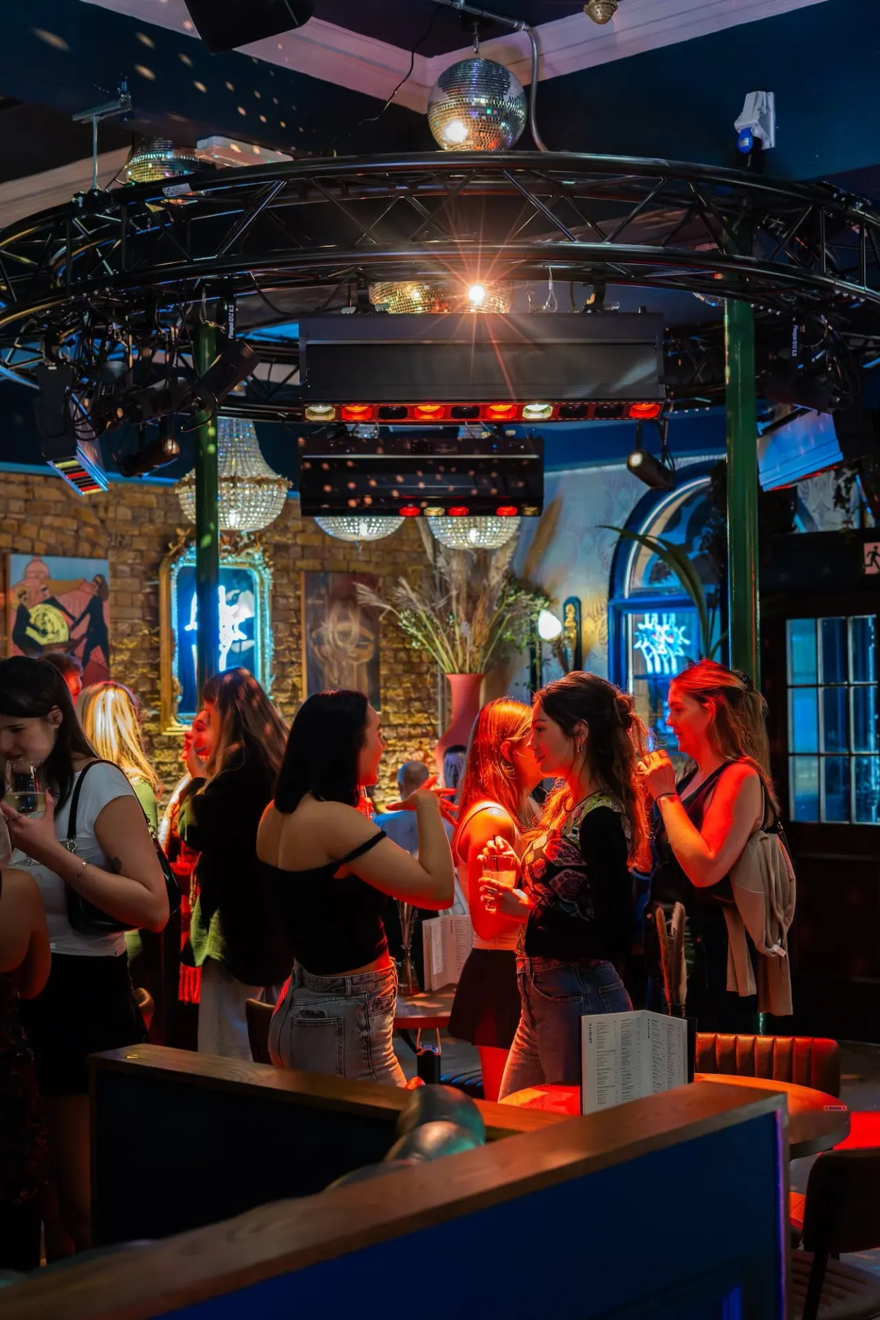 Group of people dancing and socialising under disco lighting and a mirrored ball in an indoor nightclub venue.