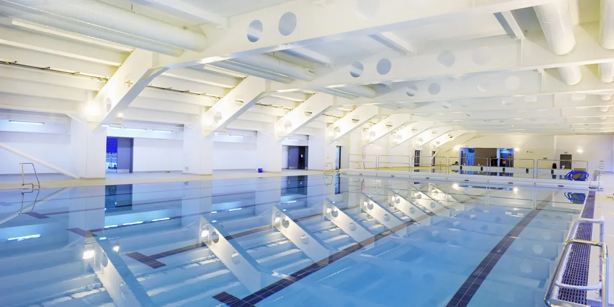 Indoor swimming pool with multiple lanes separated by dividers, brightly lit modern facility with white ceiling and support beams.