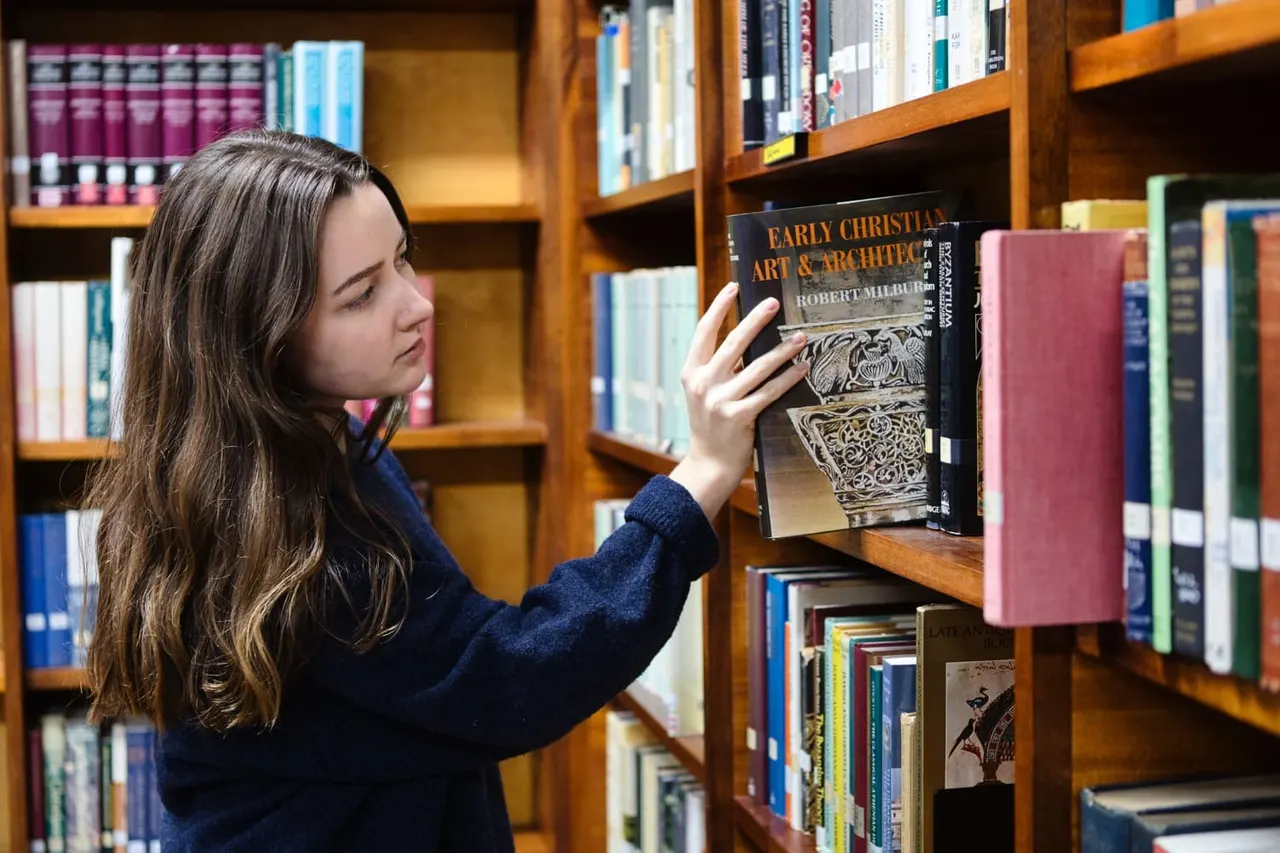 Woman selecting a book about Early Christian art and architecture from wooden library shelves.